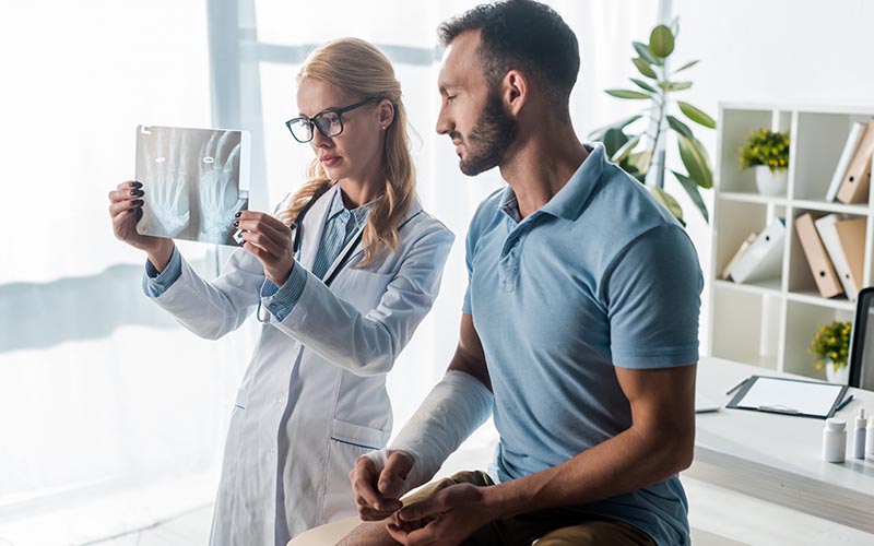 Doctor showing an injiured man his X-Rays - Common Orthopedic Injuries To Avoid This Summer